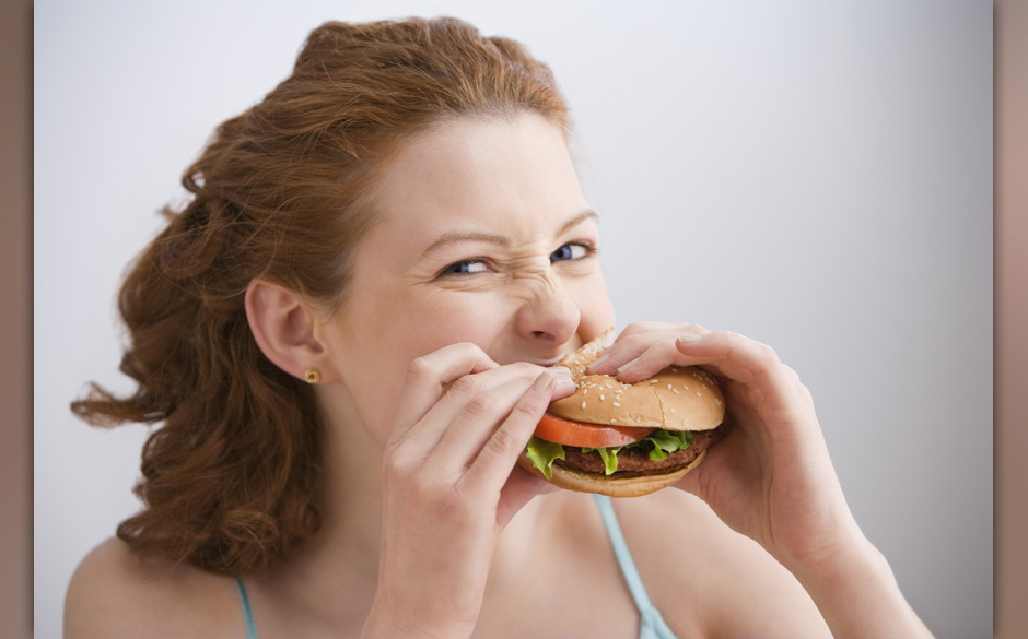 Young woman eating hamburger, portrait, close-up
