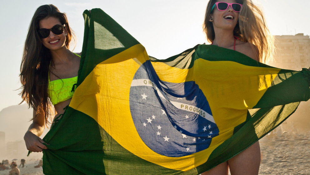 Two young women having fun on beach with Brazilian Flag