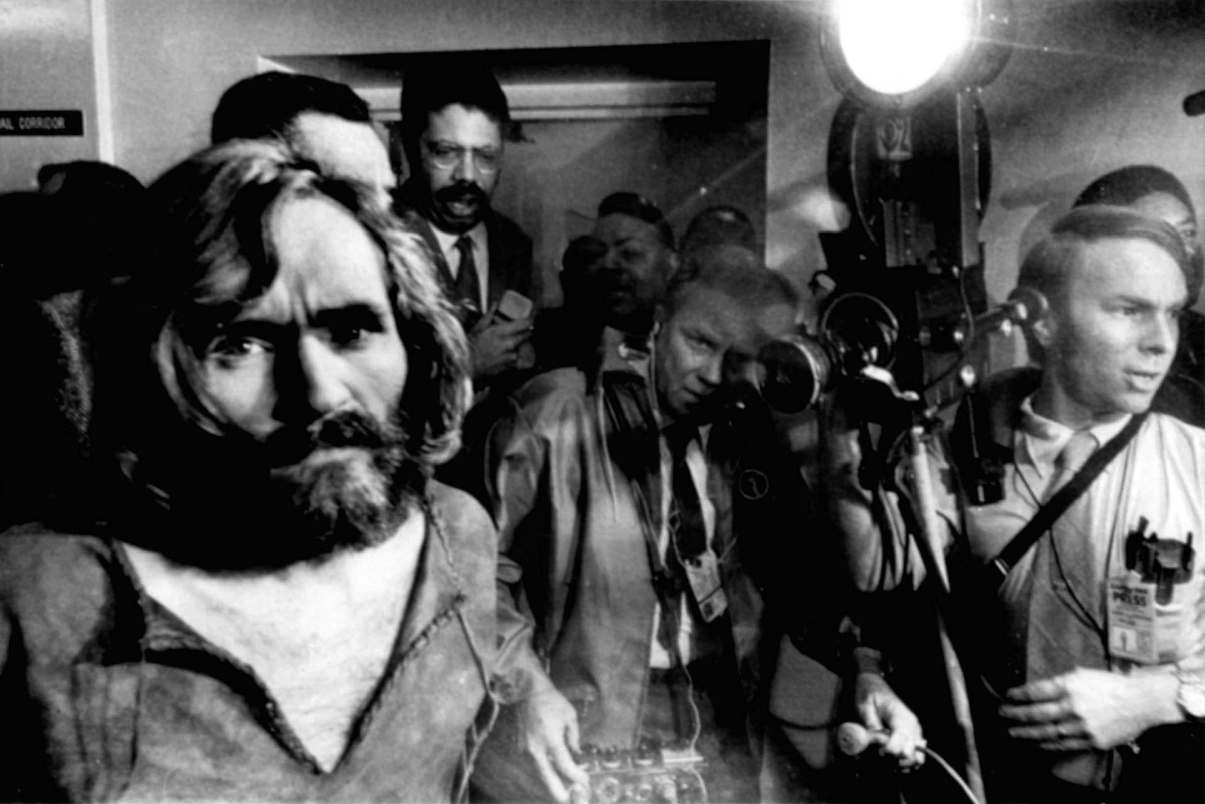 Charles Manson, the 35-year-old cult leader, is escorted through a crowd of newsmen as he arrives at the Los Angeles city ...
