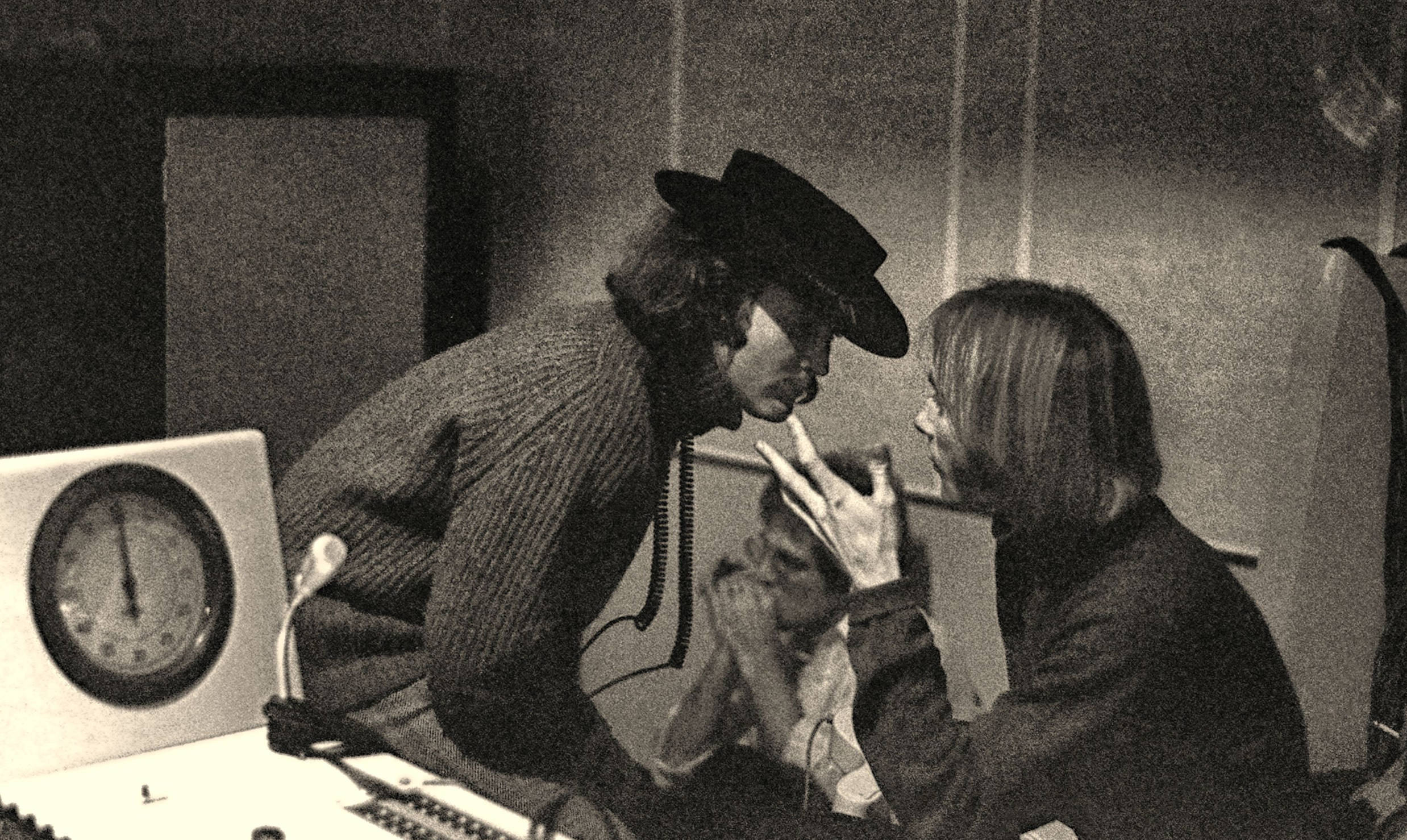 David Crosby talking to Stephen Stills while John Sebastian plays the harmonica, seen from the recording booth, looking in...