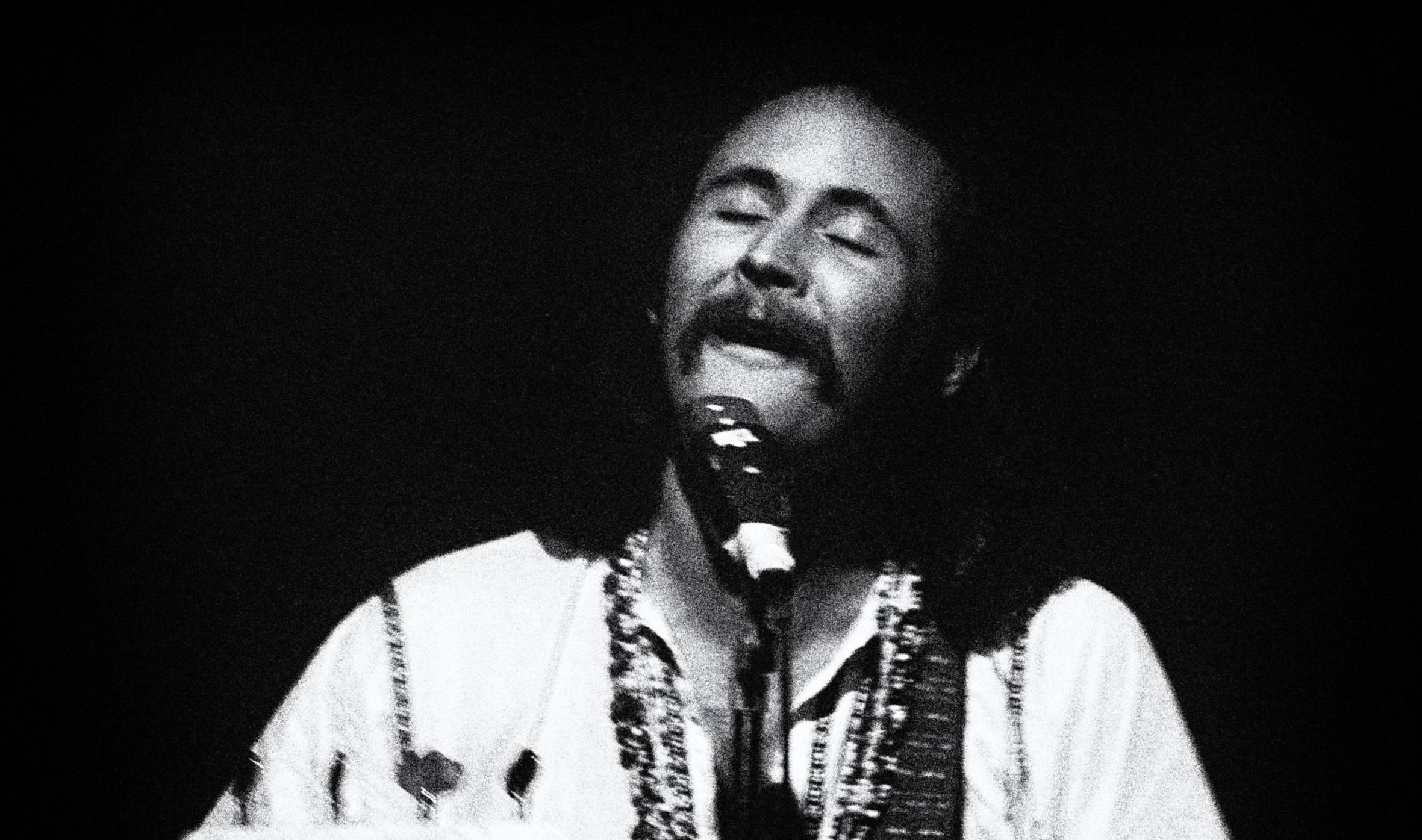 David Crosby of rock band “The Byrds” smiling as he performs in a club in a frontal, waist-high view, eyes half closed...