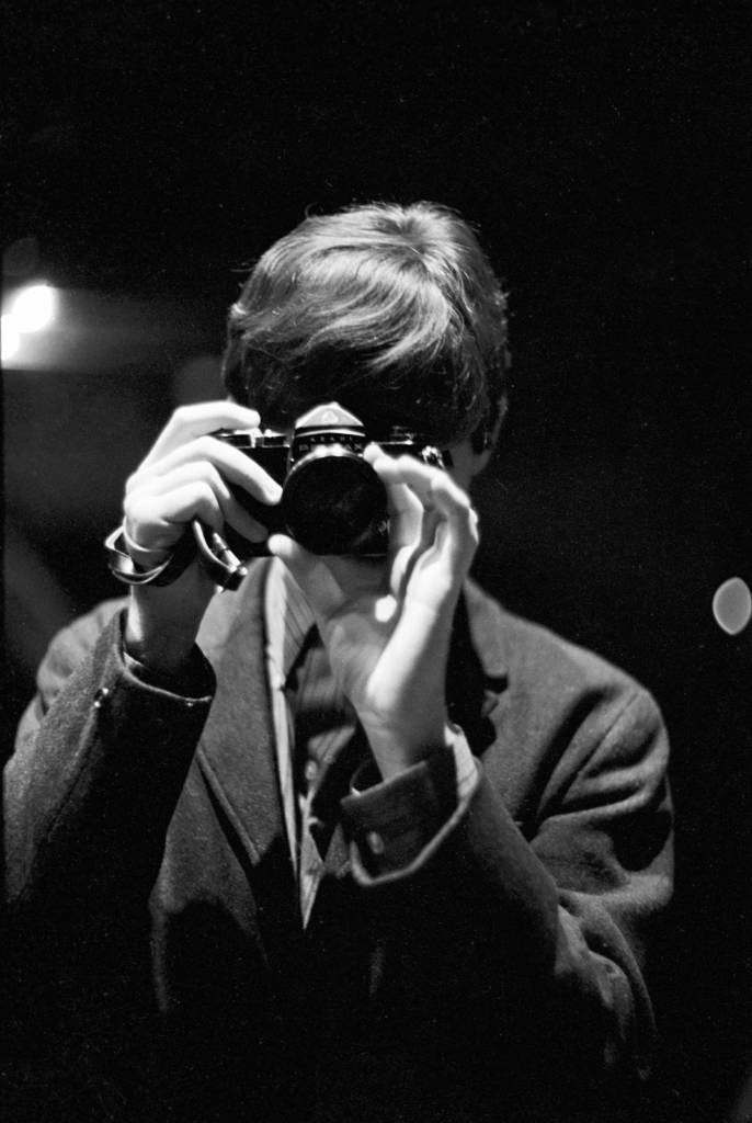 Paul McCartney hält sich eine Kamera vors Gesicht und fotografiert, wie er abgelichtet wird.