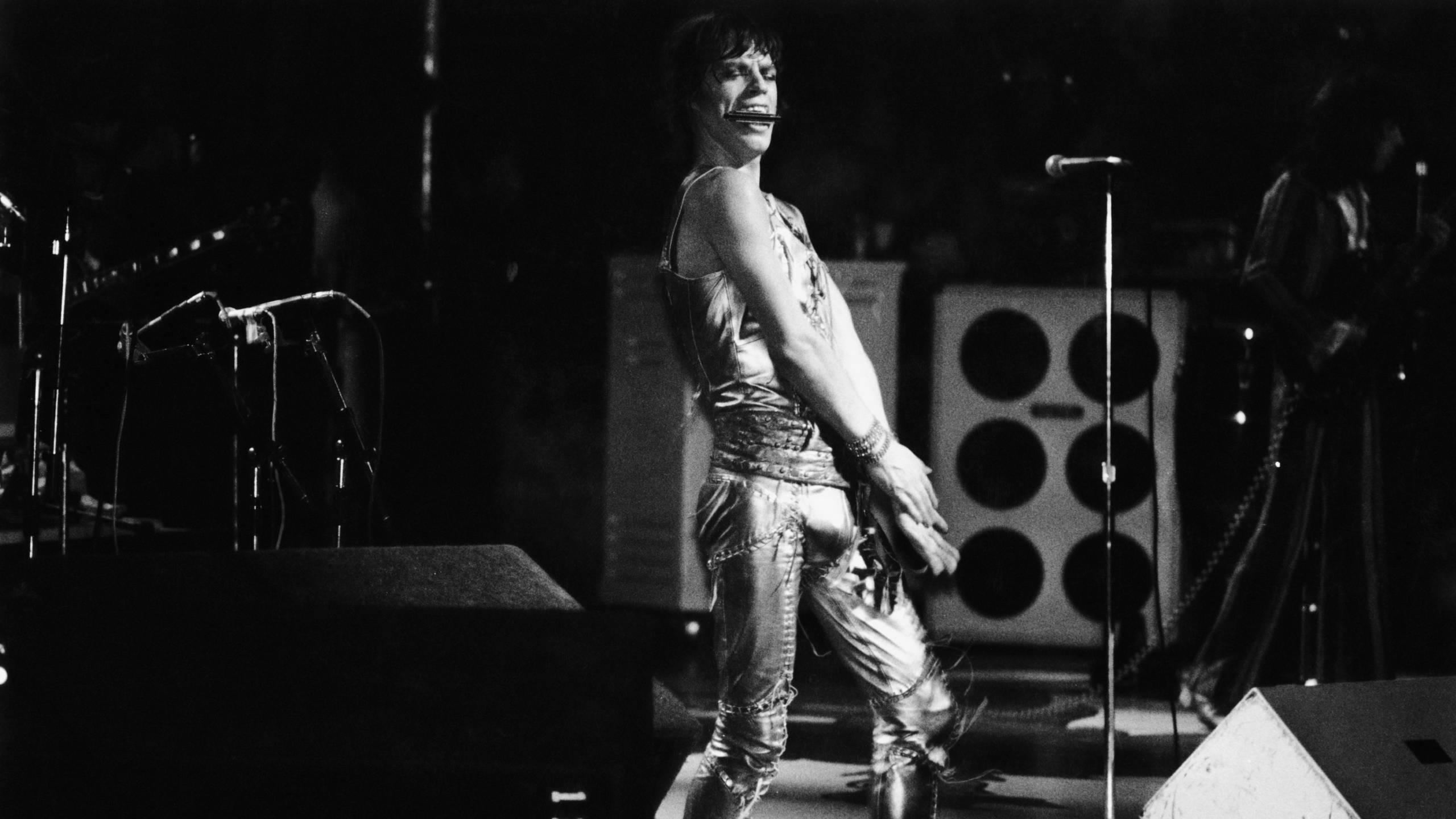Mick Jagger steht auf der Bühne. Er hält seine Mundharmonika zwischen den Zähnen.