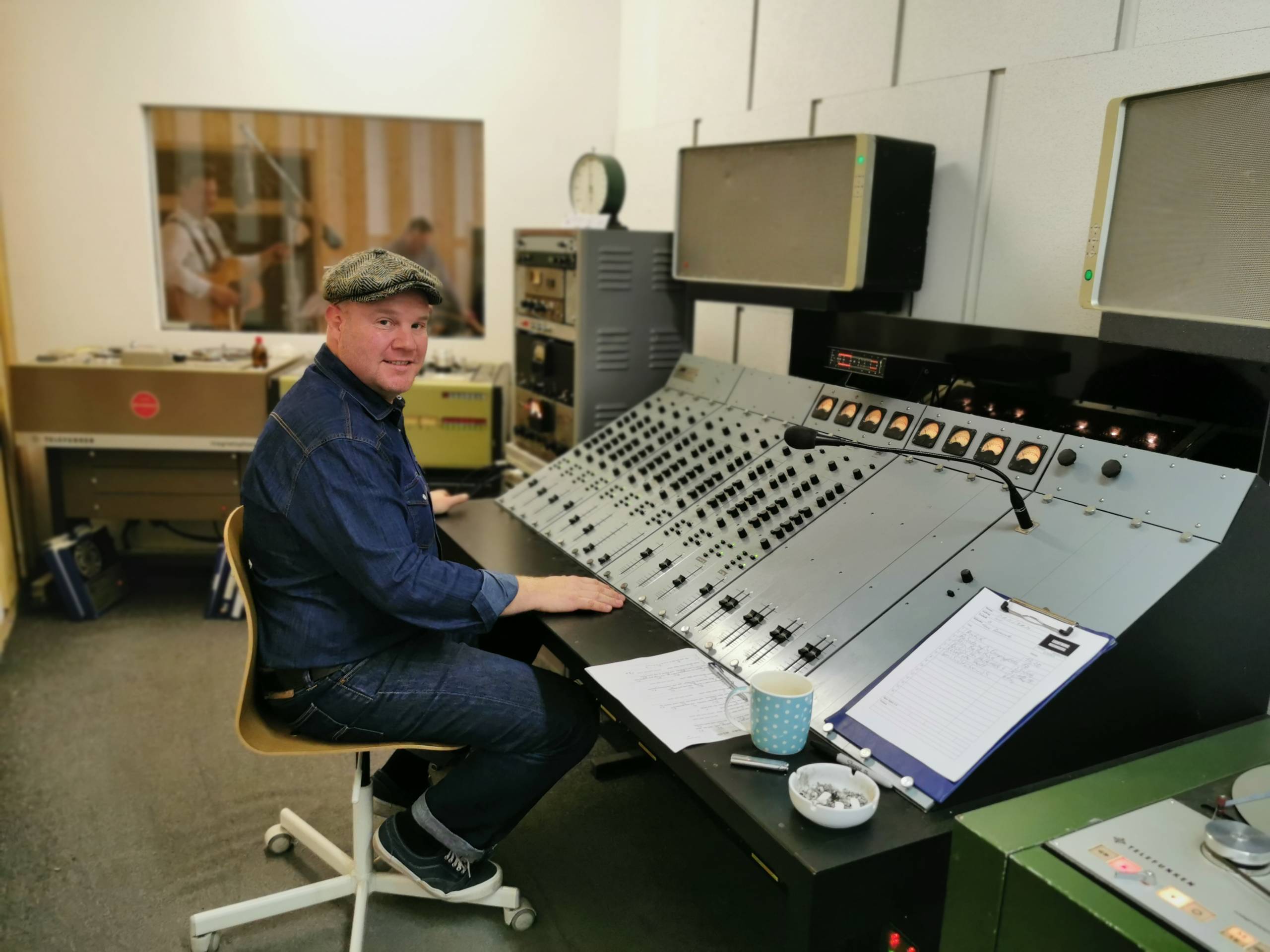 Ike Stoye sitzt in der Regie des analogen Tonstudios „Lightning Recorders“. Im Aufnahmeraum hinter ihm, spielt ein Mus...