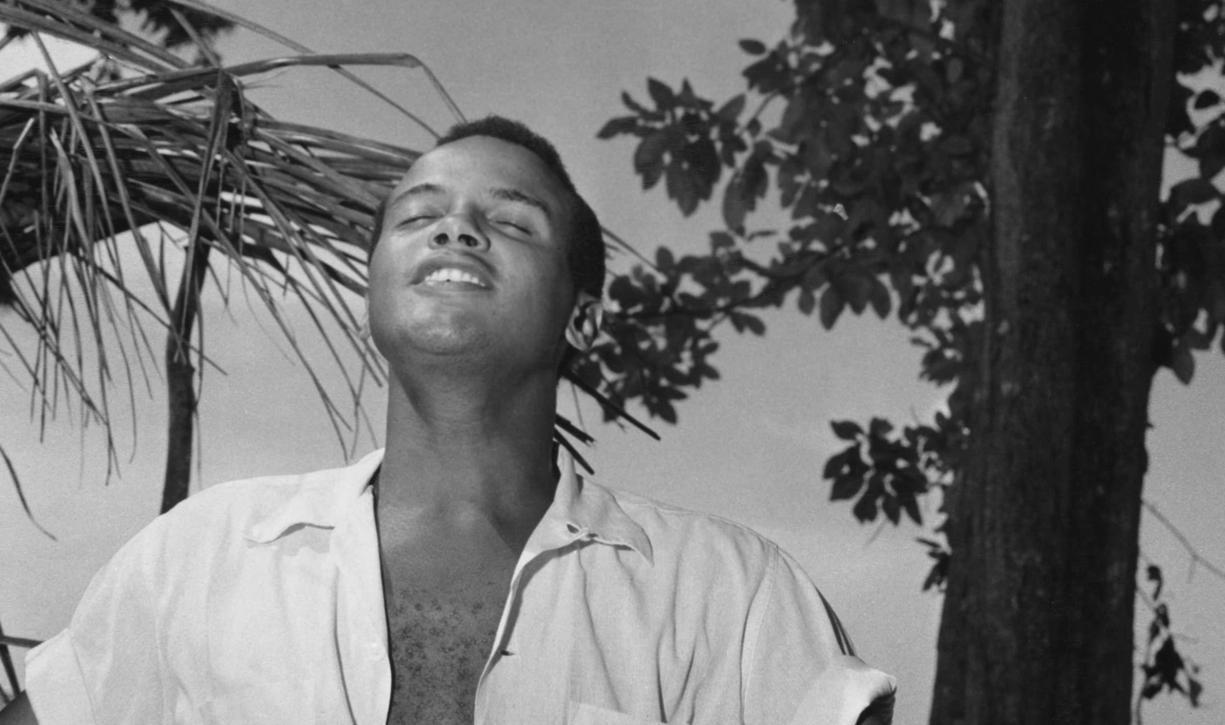 American singer-songwriter and civil rights activist Harry Belafonte stands with his short sleeve shirt open, exposing his...