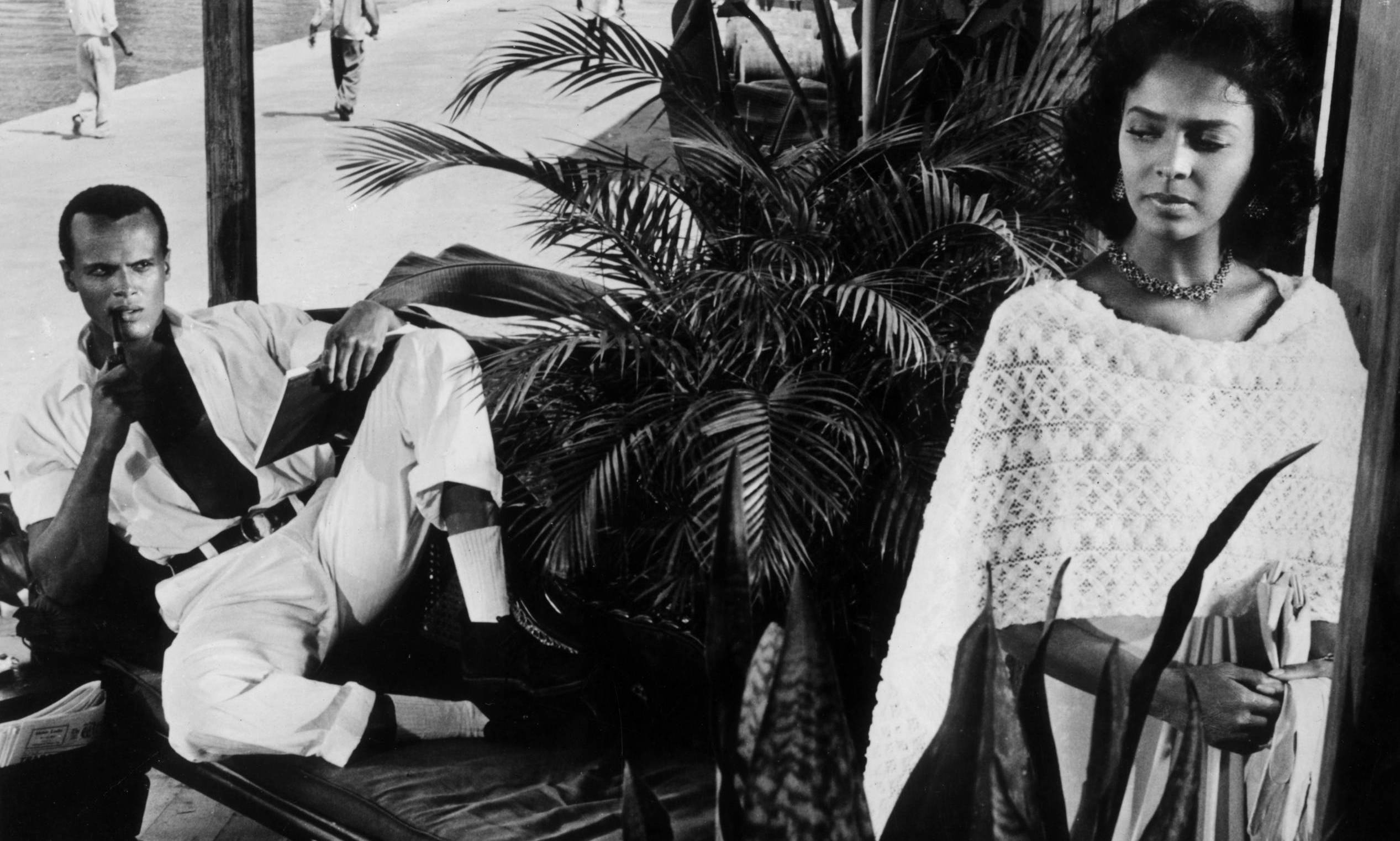 1957:  American actor and singer Harry Belafonte sitting on a divan and staring at American actor Dorothy Dandridge in a s...