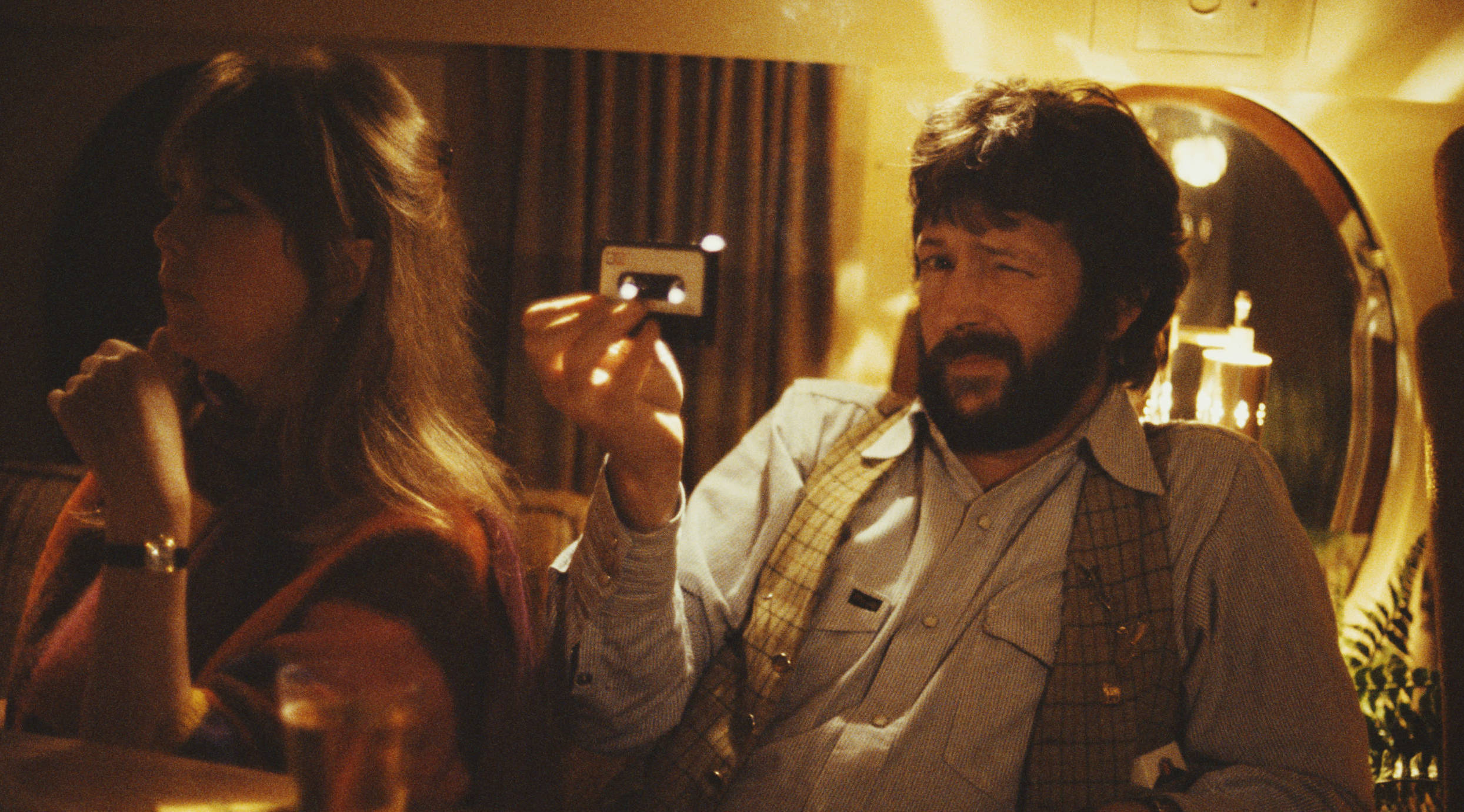 English guitarist Eric Clapton holding an audio cassette tape on board a private jet, USA, 1978. With him is his girlfriem...
