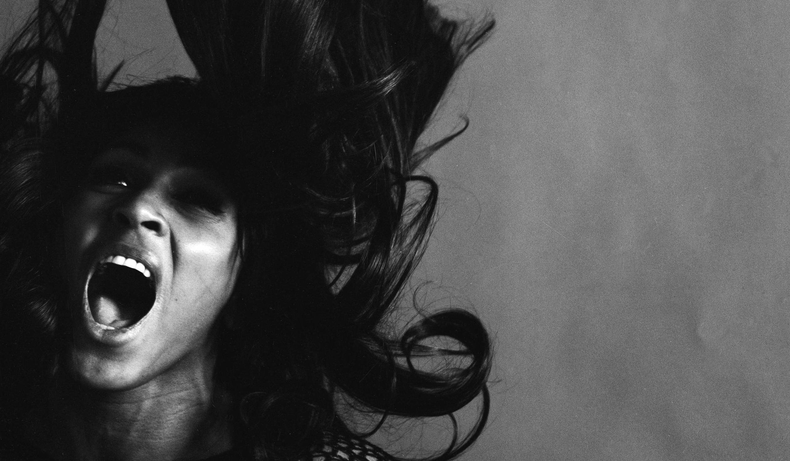 Studio portrait of American rock singer Tina Turner, wearing a dark crocheted mini-dress, singing while her long dark hair...