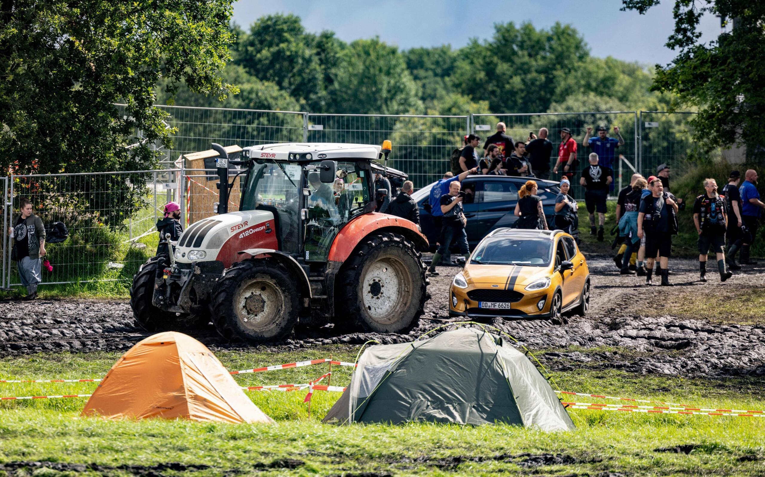 A tractor pulls a car to a parking lot on the muddy festival grounds ahead of the opening of the Wacken Open Air music fes...