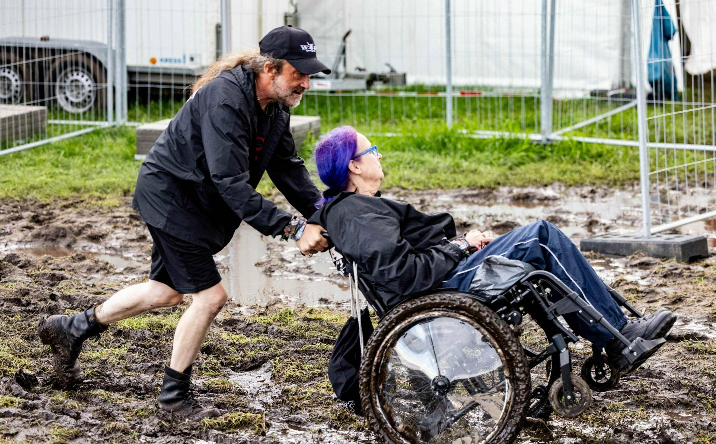 A visitor of the Wacken Open Air in a wheelchair is pushed through the mud at the festival ground on August 1, 2023. Wacke...