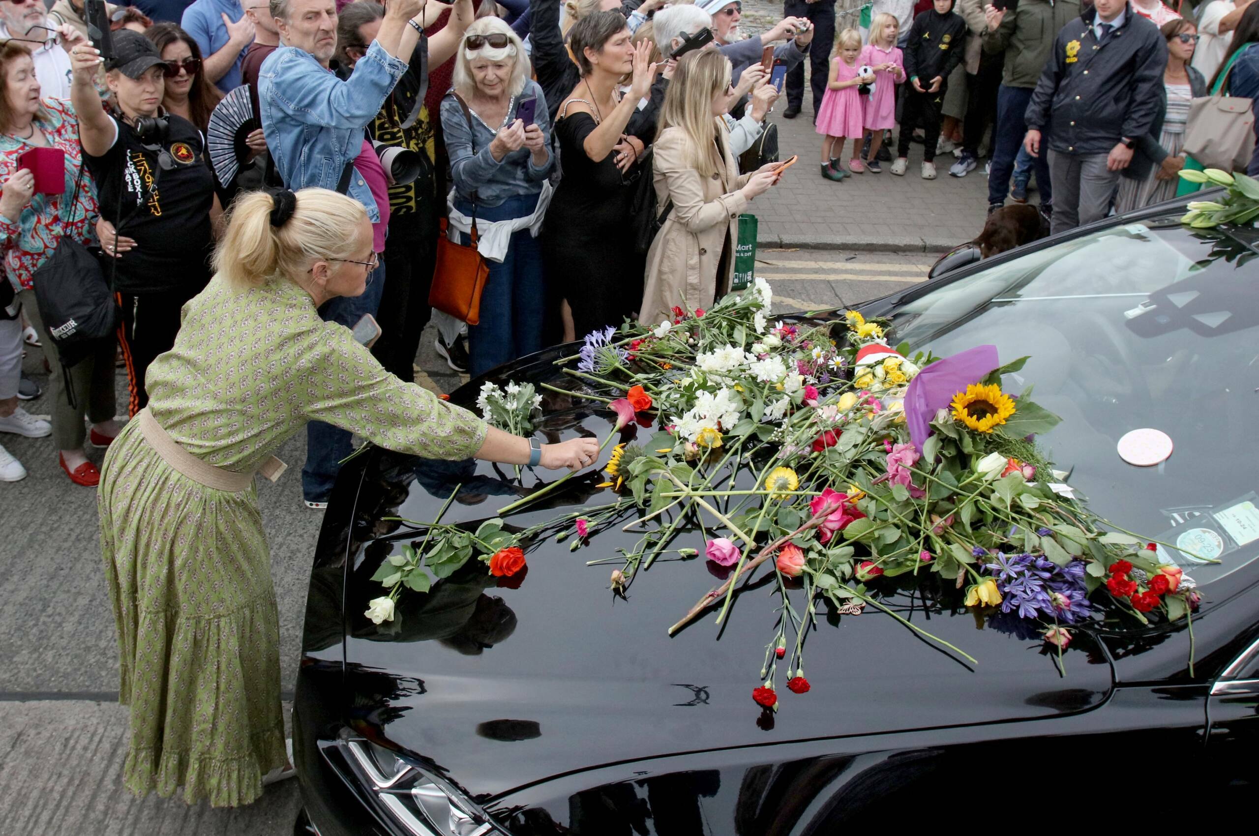 People lay flowers and tributes on the hearse during the funeral procession of late Irish singer Sinead O'Connor, outside ...