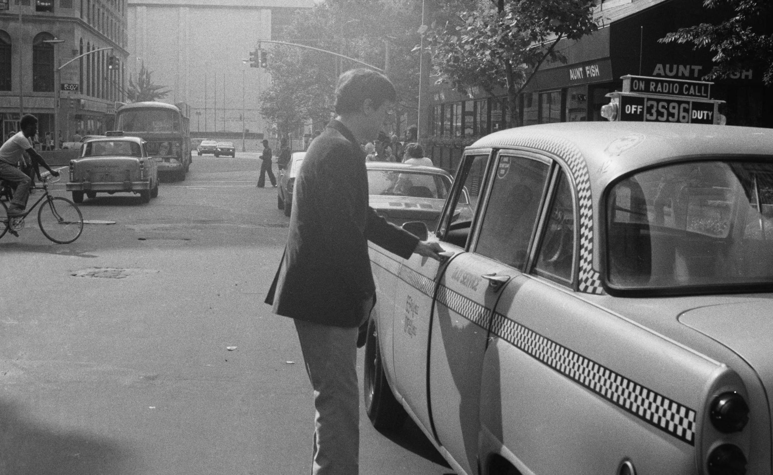 American actor Robert De Niro opening the driver's door on his Checker A series sedan cab on the set of the film 'Taxi Dri...