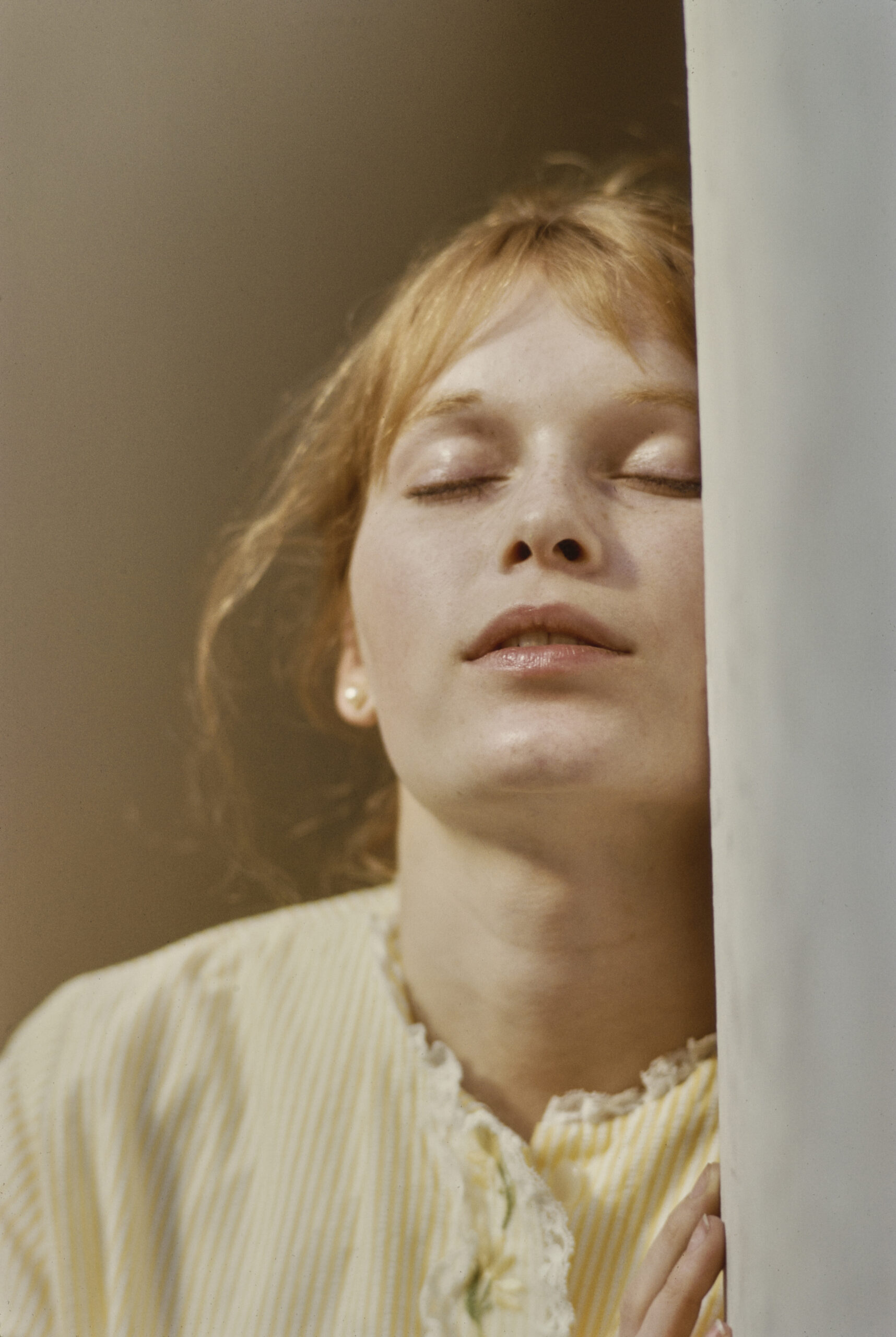 American actress Mia Farrow wearing a yellow-and-white striped outfit with a lace-trimmed neckline, with her eyes closed i...