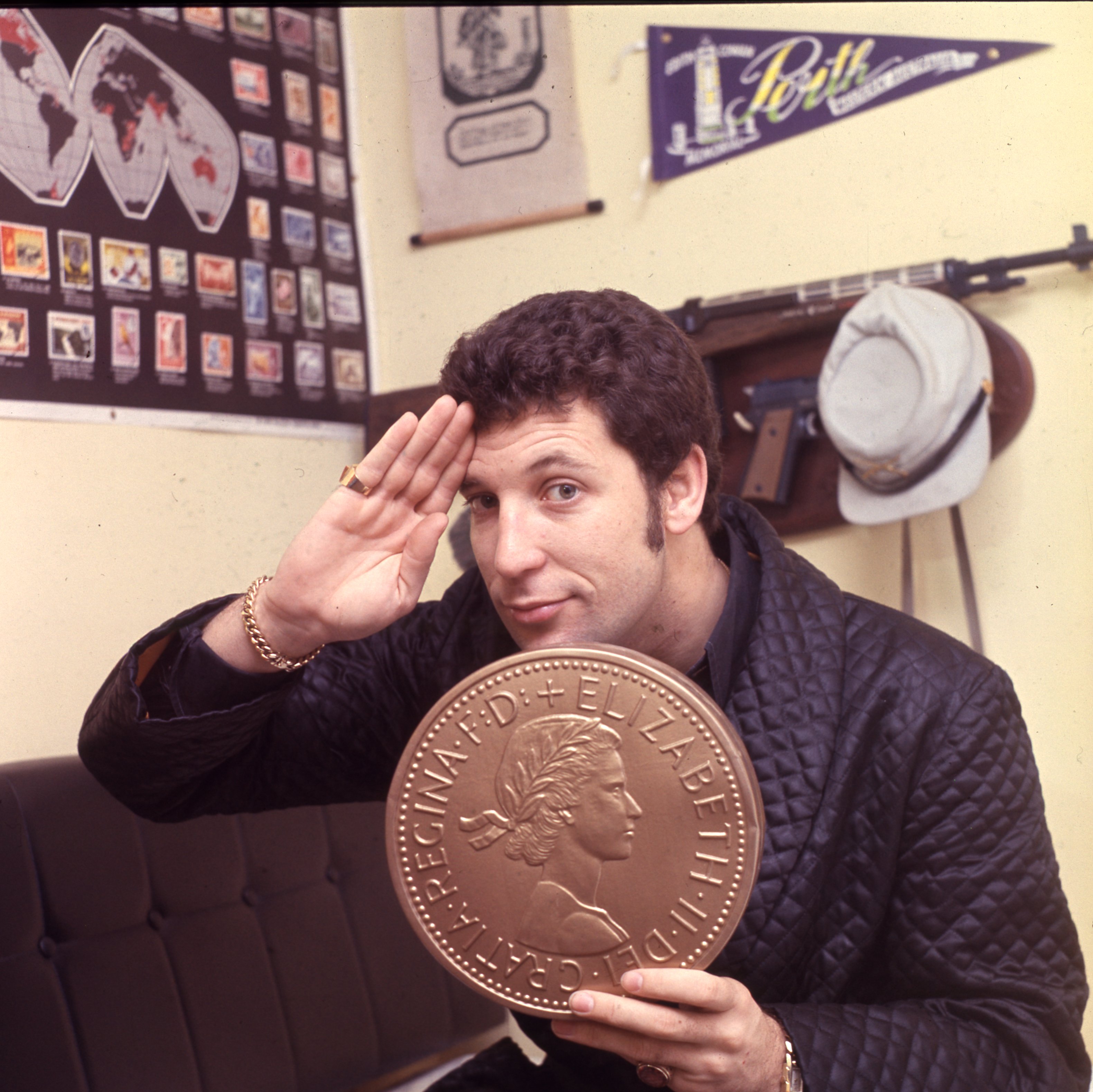 Singer Tom Jones at home, holding up a large coin, London, 1967. (Photo by Mark and Colleen Hayward/Getty Images)
