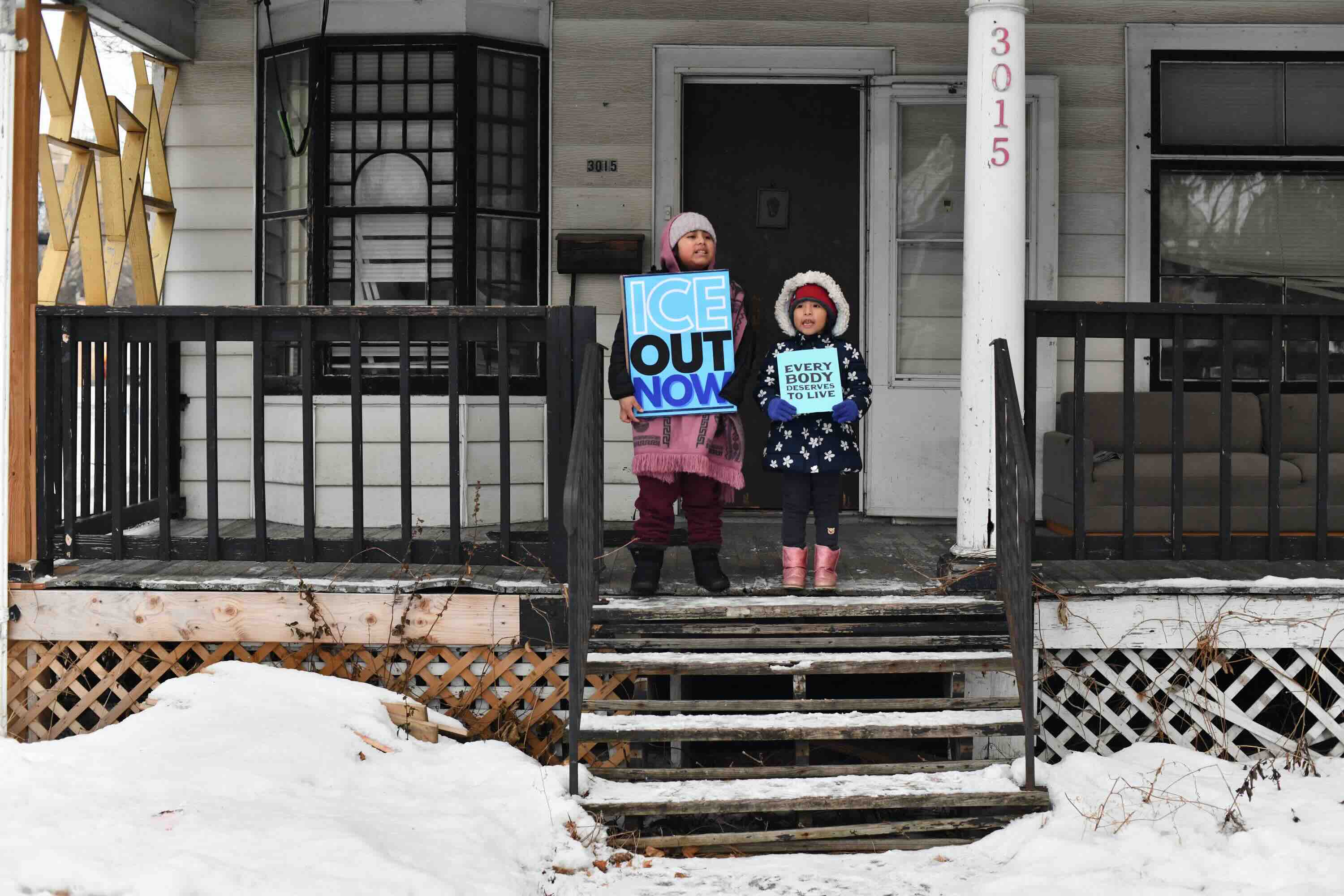 Children hold signs on the stoop of a house as protesters march from Powderhorn Park in Minneapolis against Immigration an...